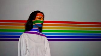 Woman standing in front of wall painted with rainbow stripes